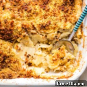 Luscious Vegan Parsnip Gratin 24 Parsnip gratin in a white baking dish, a spoon scooping out a portion.
