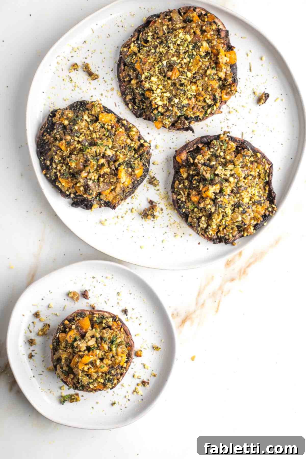 Gourmet Vegan Stuffed Portobello Mushrooms 2 Plate with three large stuffed portobello mushrooms, beautifully garnished and ready to be served. One mushroom is on a separate individual plate.