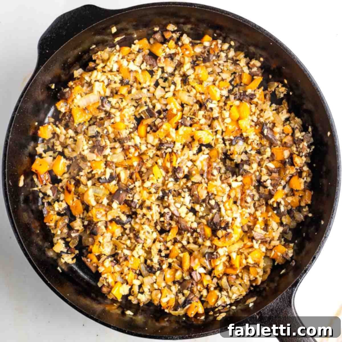 Gourmet Vegan Stuffed Portobello Mushrooms 12 Diced vegetables in a cast iron skillet with garlic and cauliflower rice added, simmering together.