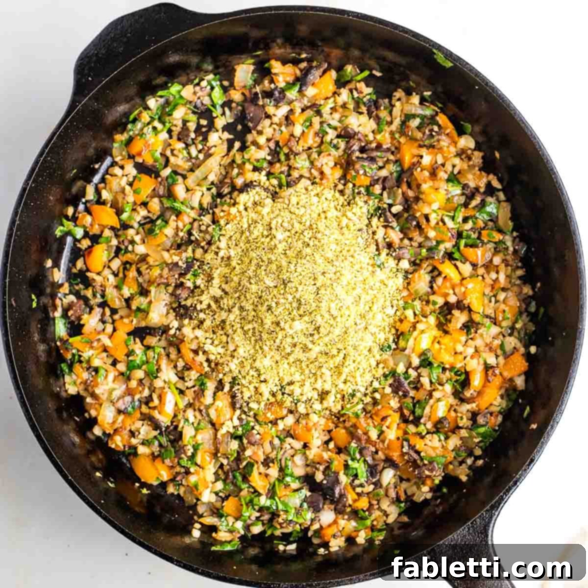 Gourmet Vegan Stuffed Portobello Mushrooms 14 Sautéed diced vegetables and greens in a cast iron skillet with a heap of yellow powder (vegan parmesan) in the center.