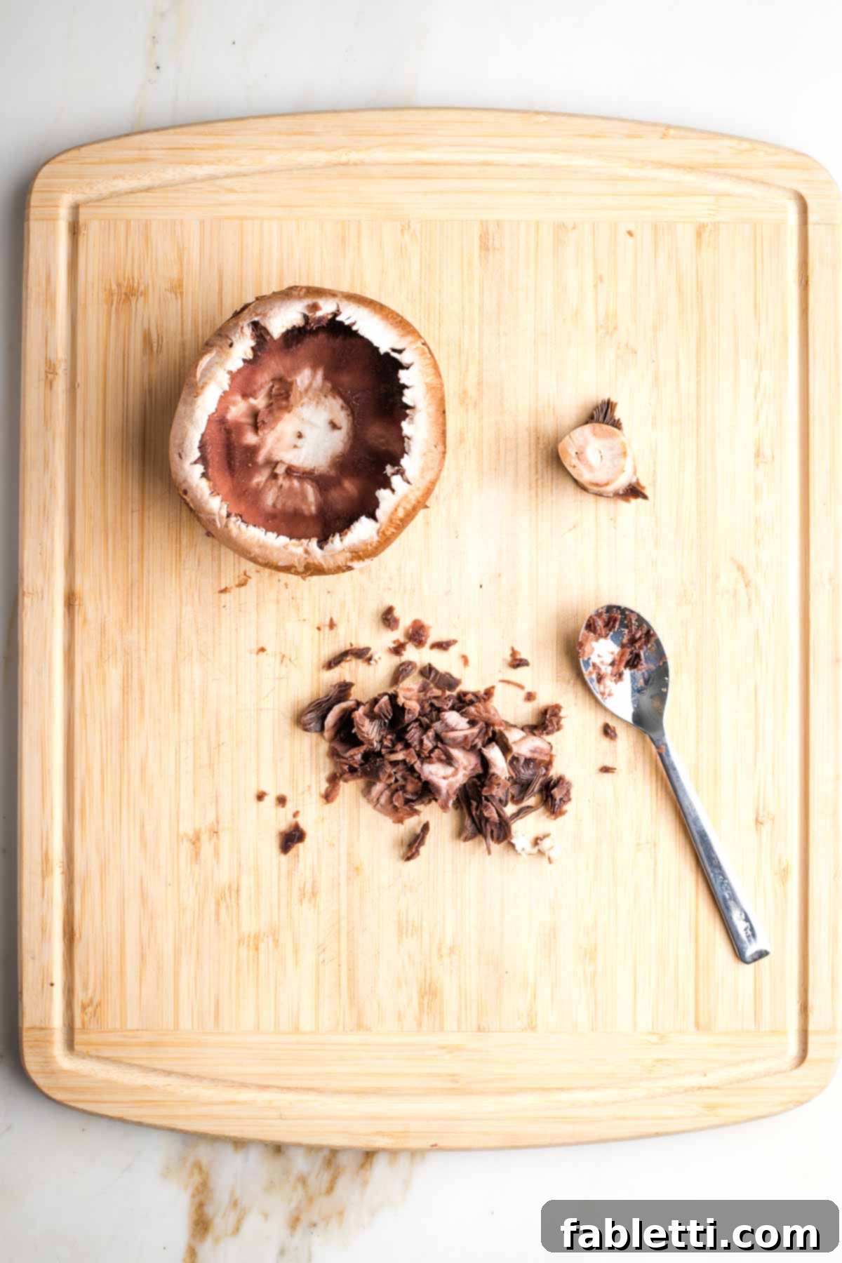 Gourmet Vegan Stuffed Portobello Mushrooms 6 Mushroom cap turned upside down with the stem on the side and a spoon with scooped out mushroom gills, illustrating the preparation process.