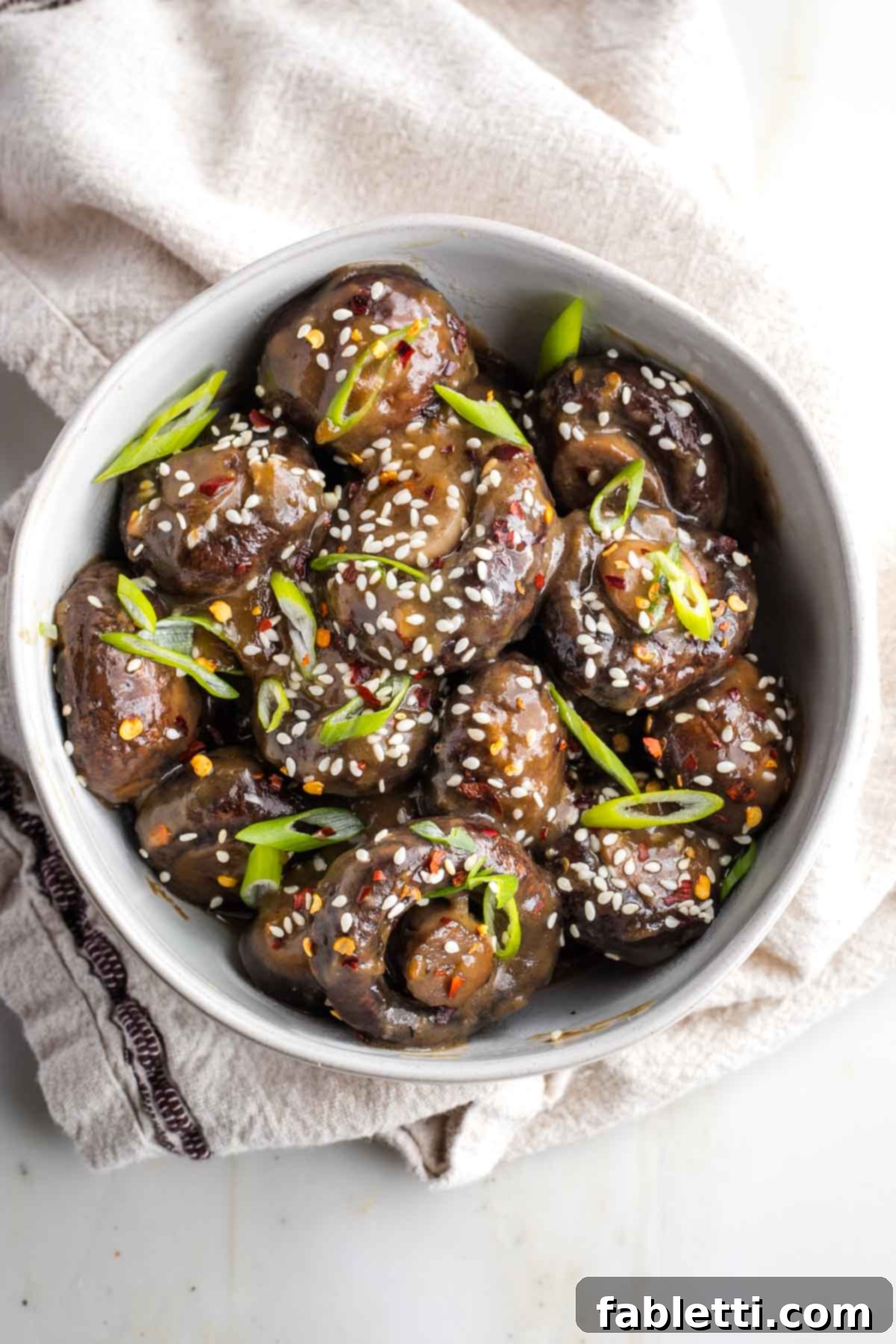 Umami-Rich Vegan Miso Mushrooms 12 Bowl of saucy mushrooms garnished with sesame seeds, scallions and red pepper flakes.