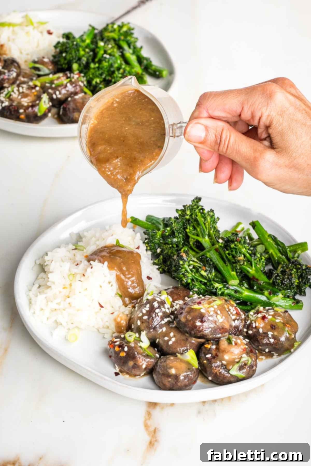 Umami-Rich Vegan Miso Mushrooms 13 Small pitcher of sauce pouring over rice on a plate with mushrooms and broccolini.