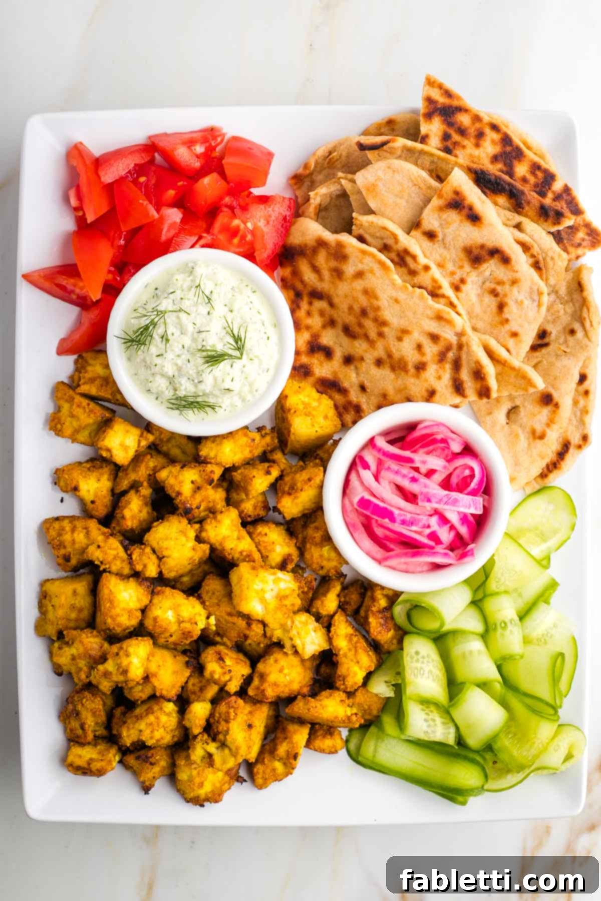 Flavorful Vegan Tofu Shawarma 2 A beautifully arranged platter showcasing crispy tofu shawarma, warm pita bread, fresh cucumber and tomato salad, tangy pickled onions, and creamy tzatziki.