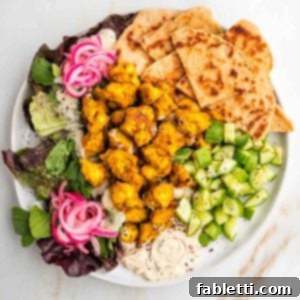 Flavorful Vegan Tofu Shawarma 12 Tofu shawarma on a plate with pita, cucumbers, hummus, pickled red onions and leafy greens.