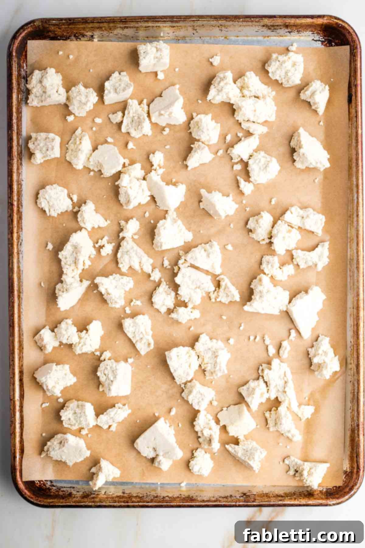 Flavorful Vegan Tofu Shawarma 7 Hands tearing a block of pressed tofu into irregular, bite-sized pieces, arranged on a baking sheet lined with parchment paper.