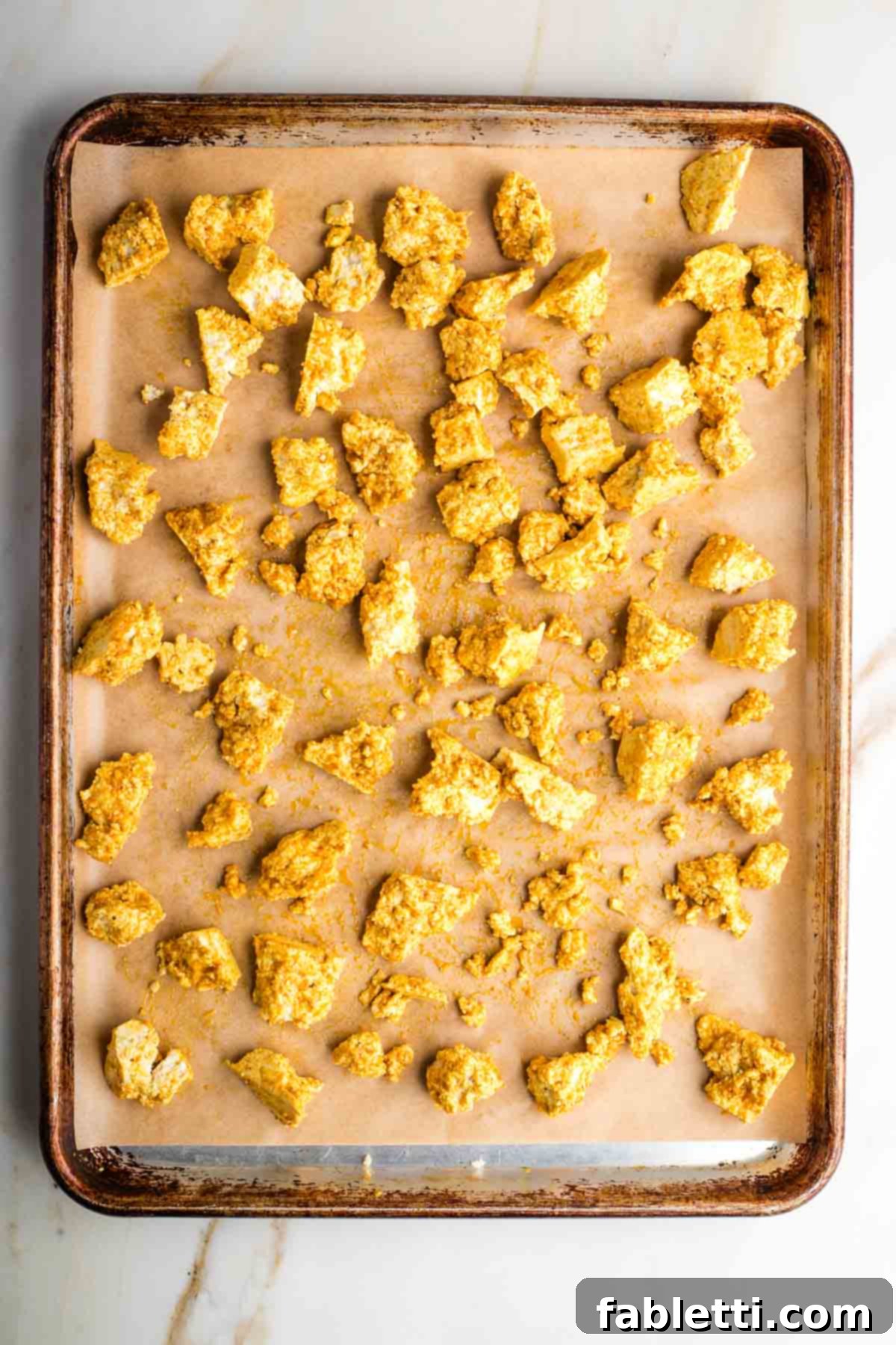 Flavorful Vegan Tofu Shawarma 8 Hands mixing torn tofu pieces with a rich, dark shawarma marinade on a parchment-lined baking sheet, ensuring every piece is evenly coated.