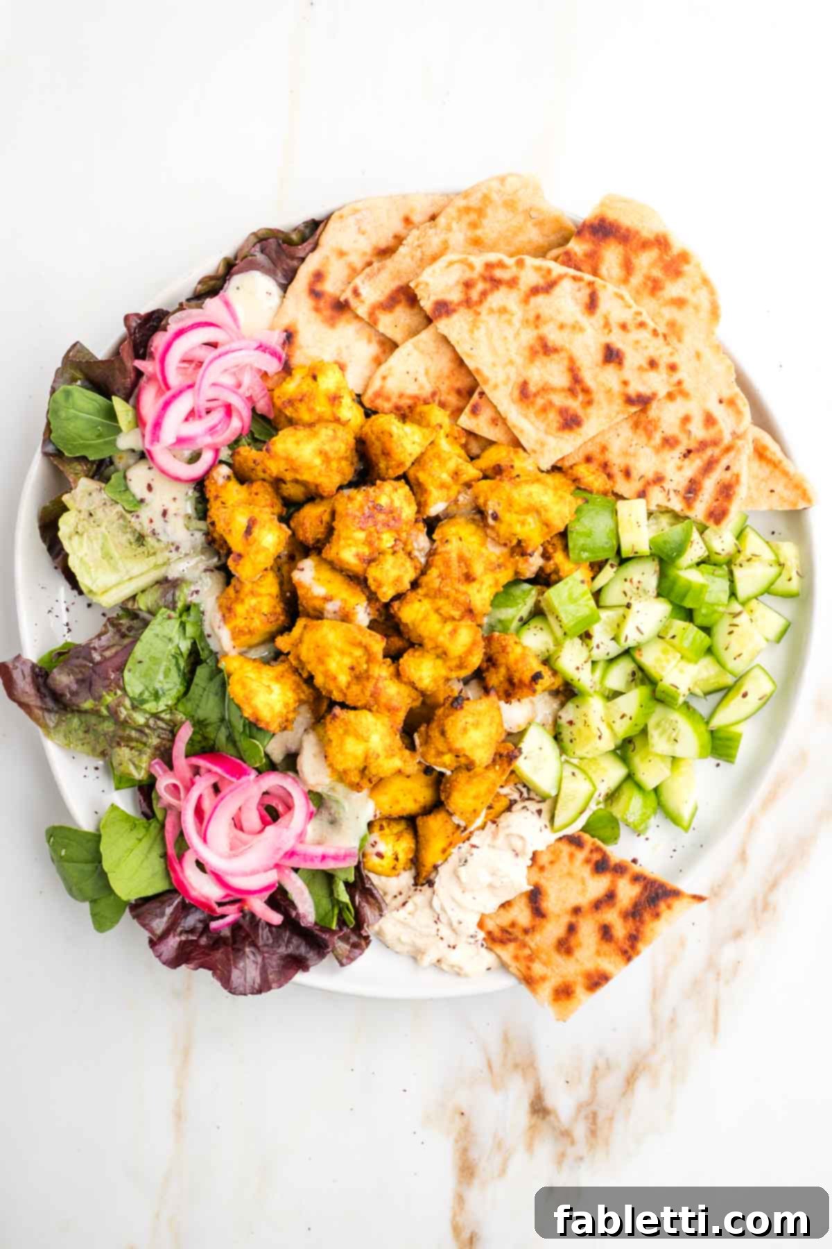 Flavorful Vegan Tofu Shawarma 10 A vibrant platter featuring a generous portion of tofu shawarma, warm pita bread, crisp lettuce, bright pickled onions, creamy hummus, and refreshing cucumber slices, ready for serving.