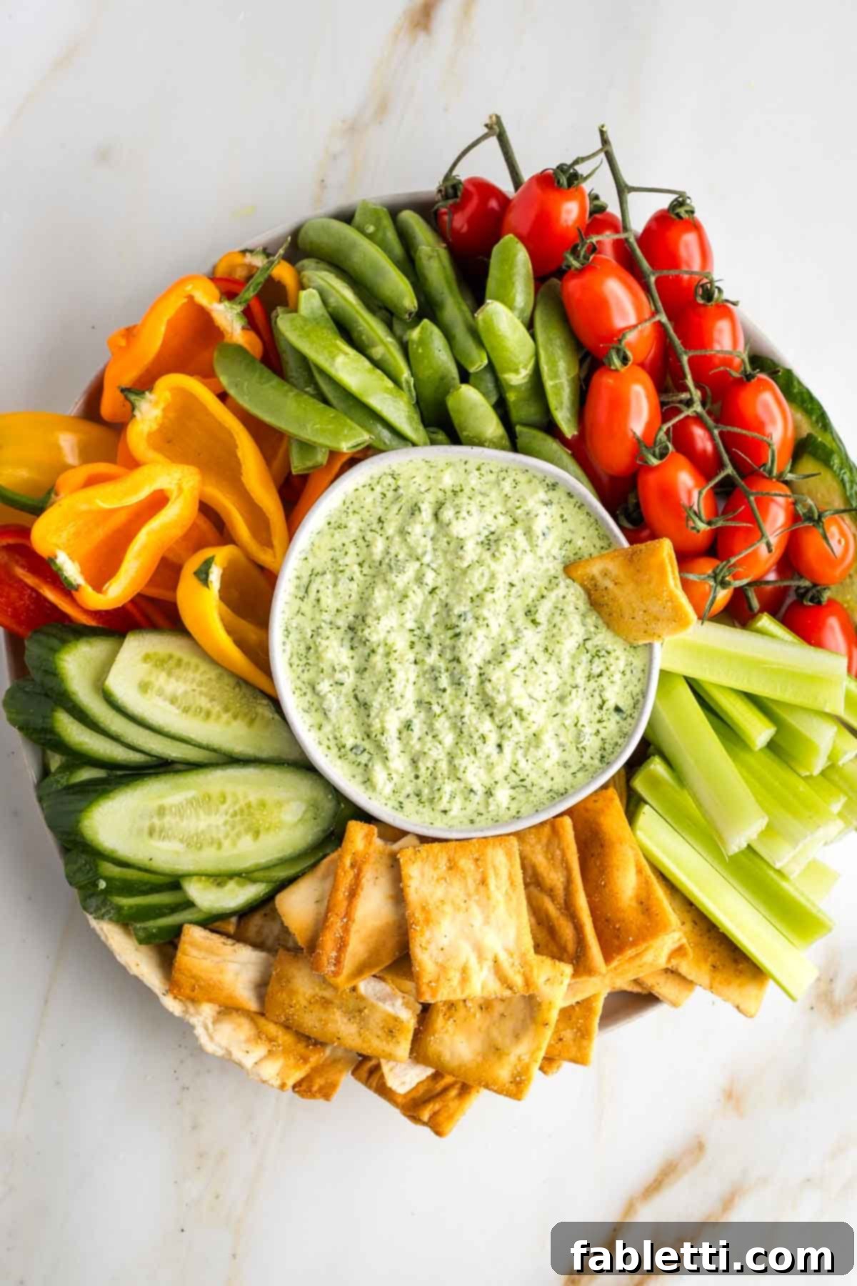 Vegan Tzatziki Sauce 2 Green tzatziki dip in a bowl, surrounded by colorful veggies on a platter.