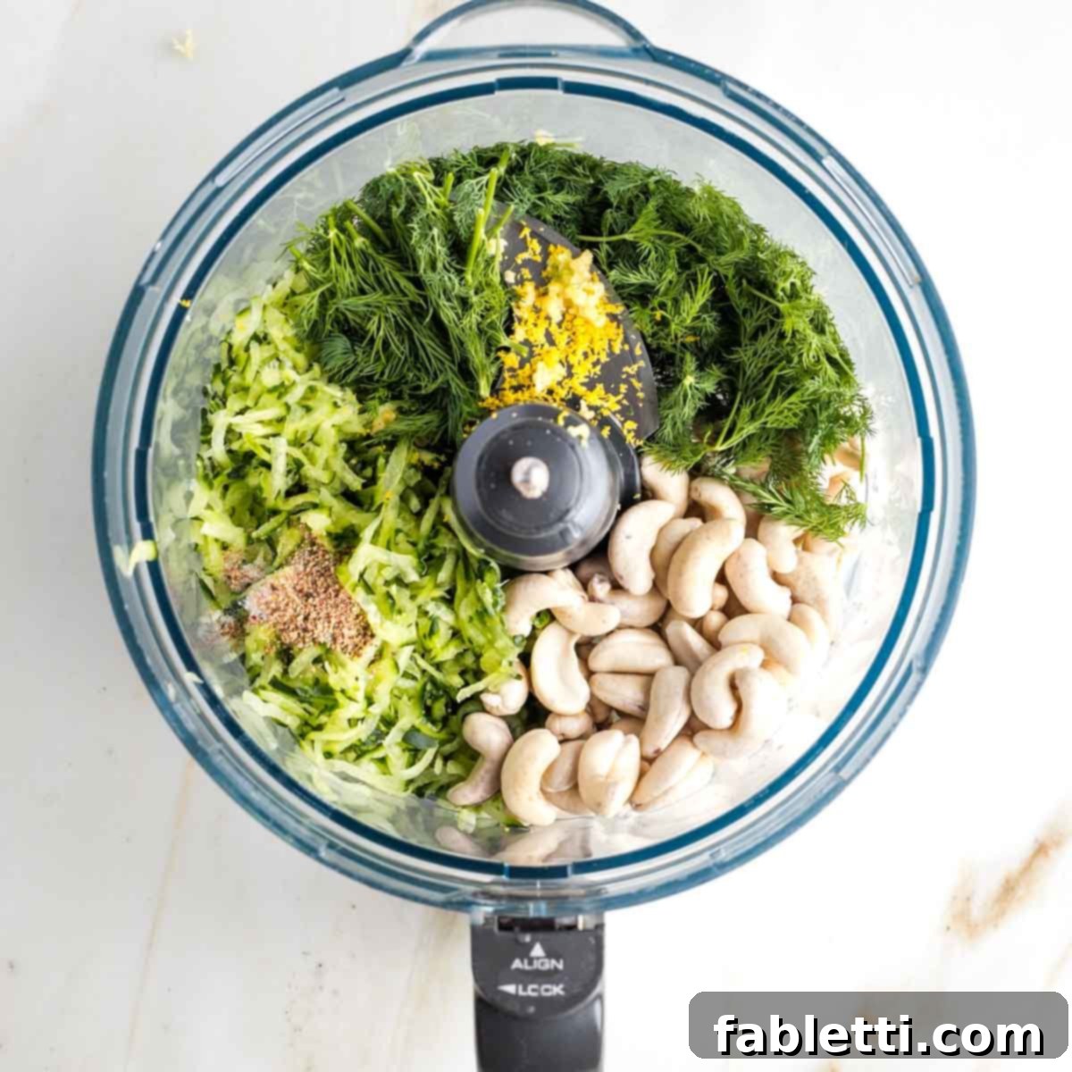 Vegan Tzatziki Sauce 7 Ingredients for dairy-free tzatziki sauce in the bowl of a food processor: fresh herbs, grated cucumber, cashews, lemon zest and seasonings.