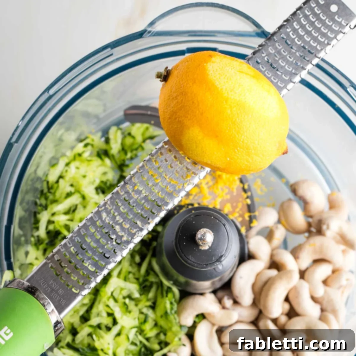 Vegan Tzatziki Sauce 10 Zesting a lemon over a food processor filled with cashews and grated cucumber.