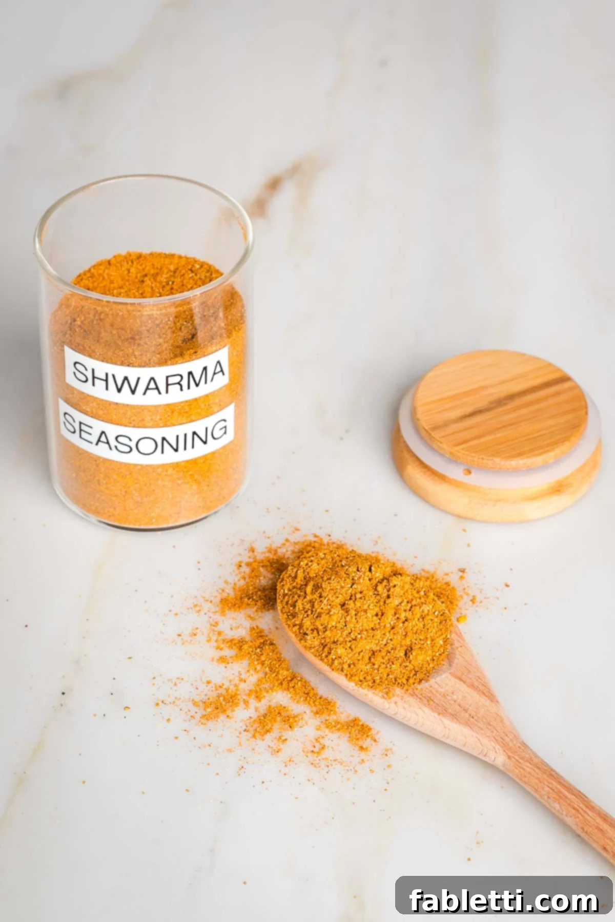 Ultimate Shawarma Spice Mix 2 Jar labeled "shwarma spice blend" filled with orangish brown powder, a spoon filled with it and the lid to the jar.