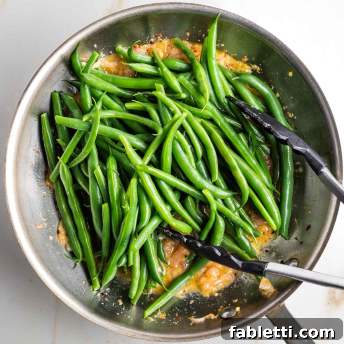 Zesty Green Bean Salad 11 A skillet containing the lemony mustard sauce, with a pile of bright green beans just added on top, ready to be tossed.