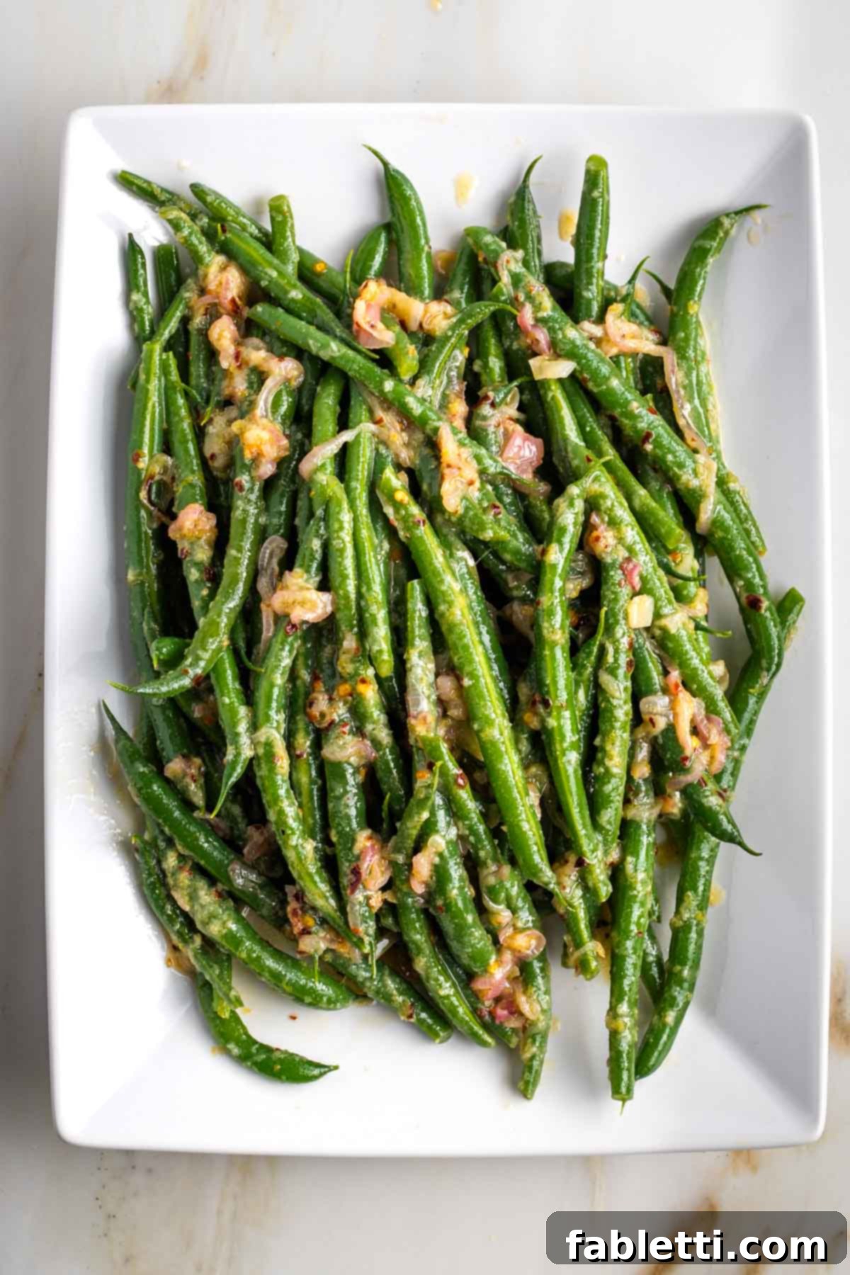 Zesty Green Bean Salad 13 A close-up of bright green beans tossed with shallots and lemon vinaigrette on a white serving platter.
