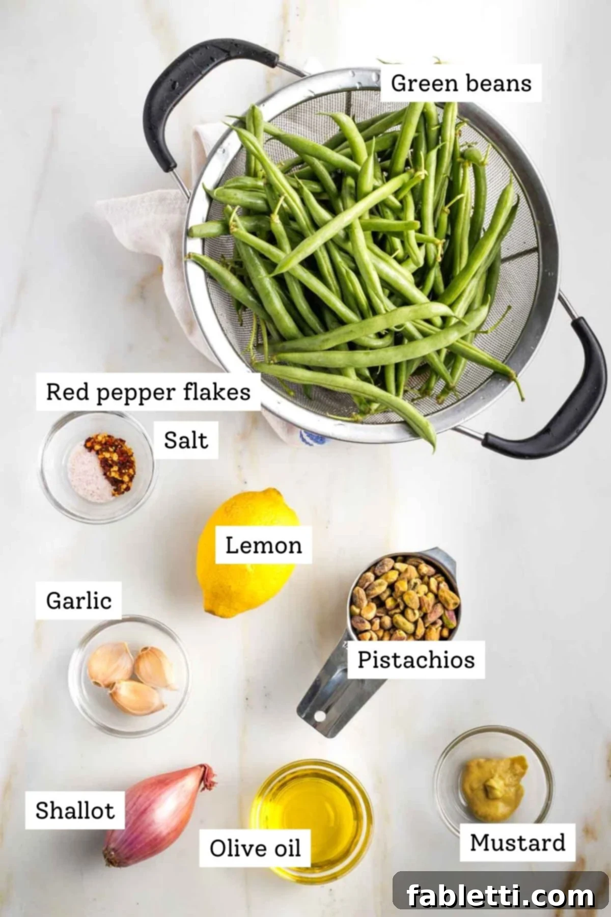 Zesty Green Bean Salad 3 Labeled ingredients for Lemony Green Bean Salad: fresh green beans, salt, pepper, lemon, shallot, pistachios, garlic, mustard, olive oil.