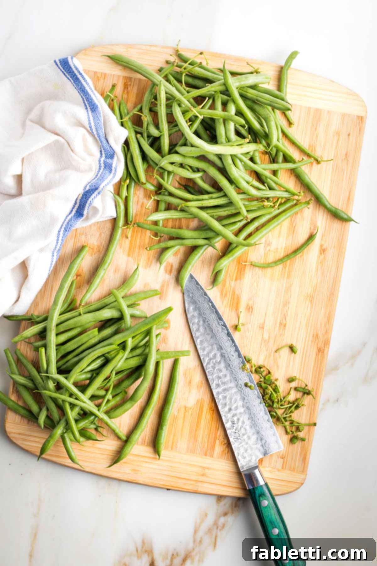 Zesty Green Bean Salad 4 Trimming the ends off fresh green beans on a wooden cutting board.