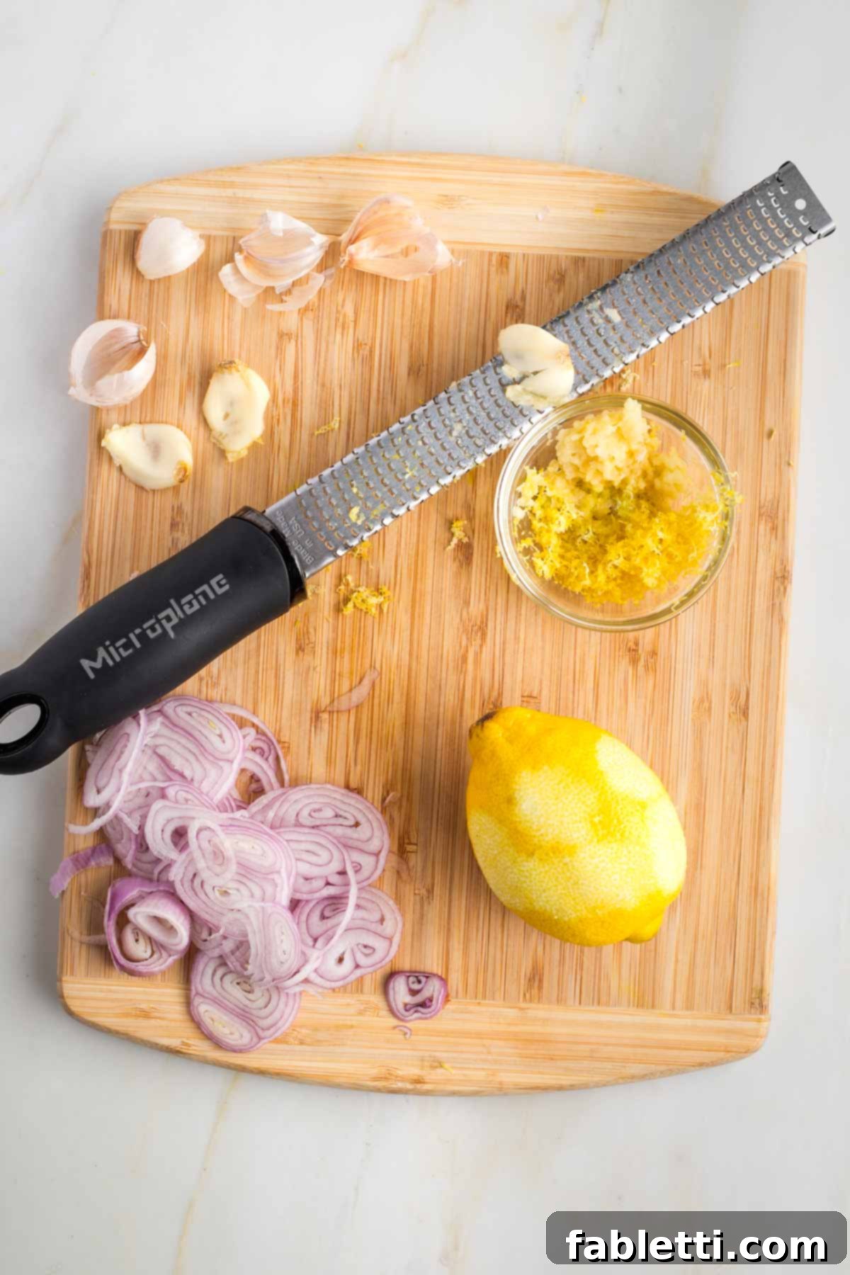 Zesty Green Bean Salad 5 Grating garlic and lemon zest with a microplane on a cutting board, alongside thinly sliced shallots.