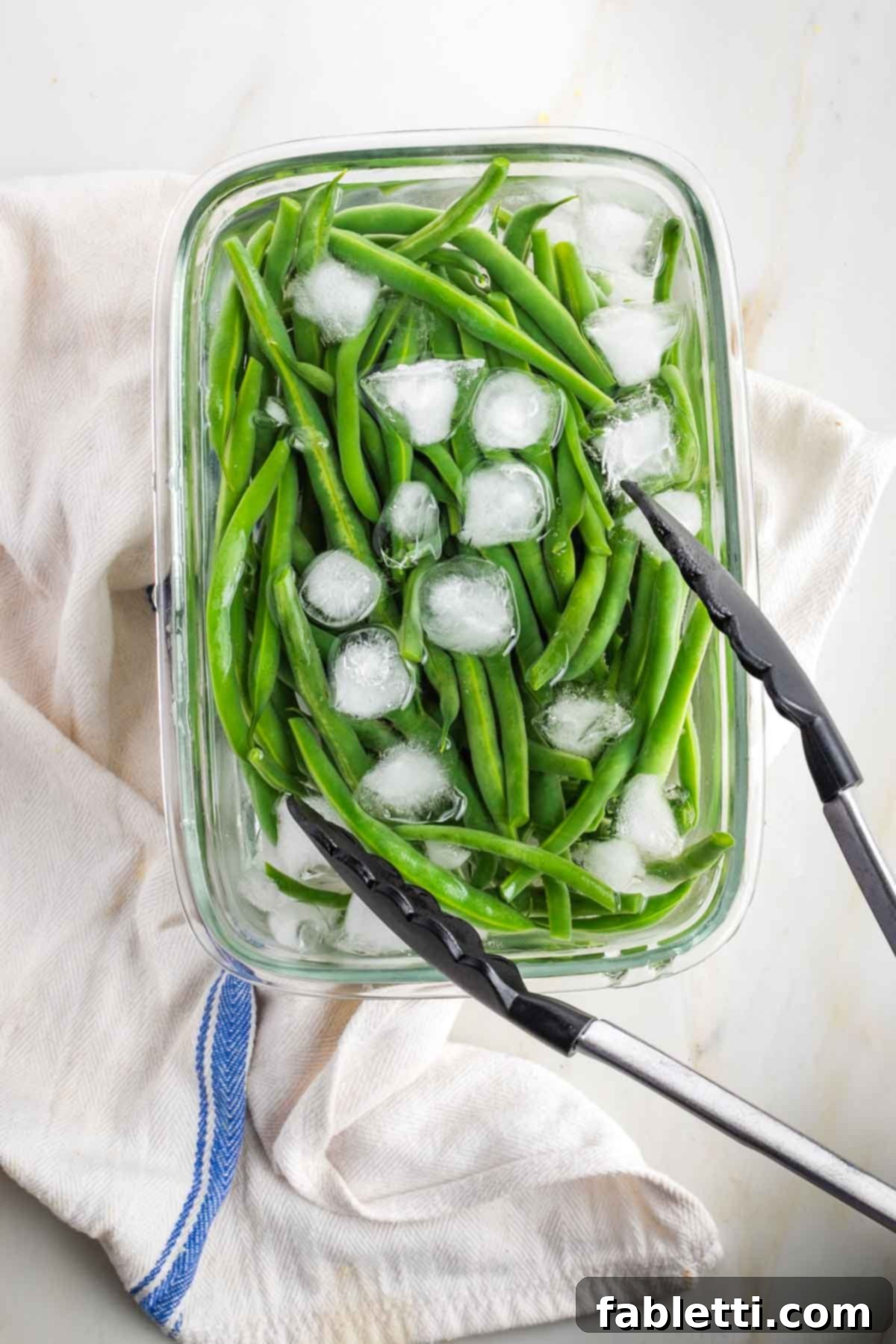 Zesty Green Bean Salad 7 Bright green beans submerged in a dish filled with ice and water.