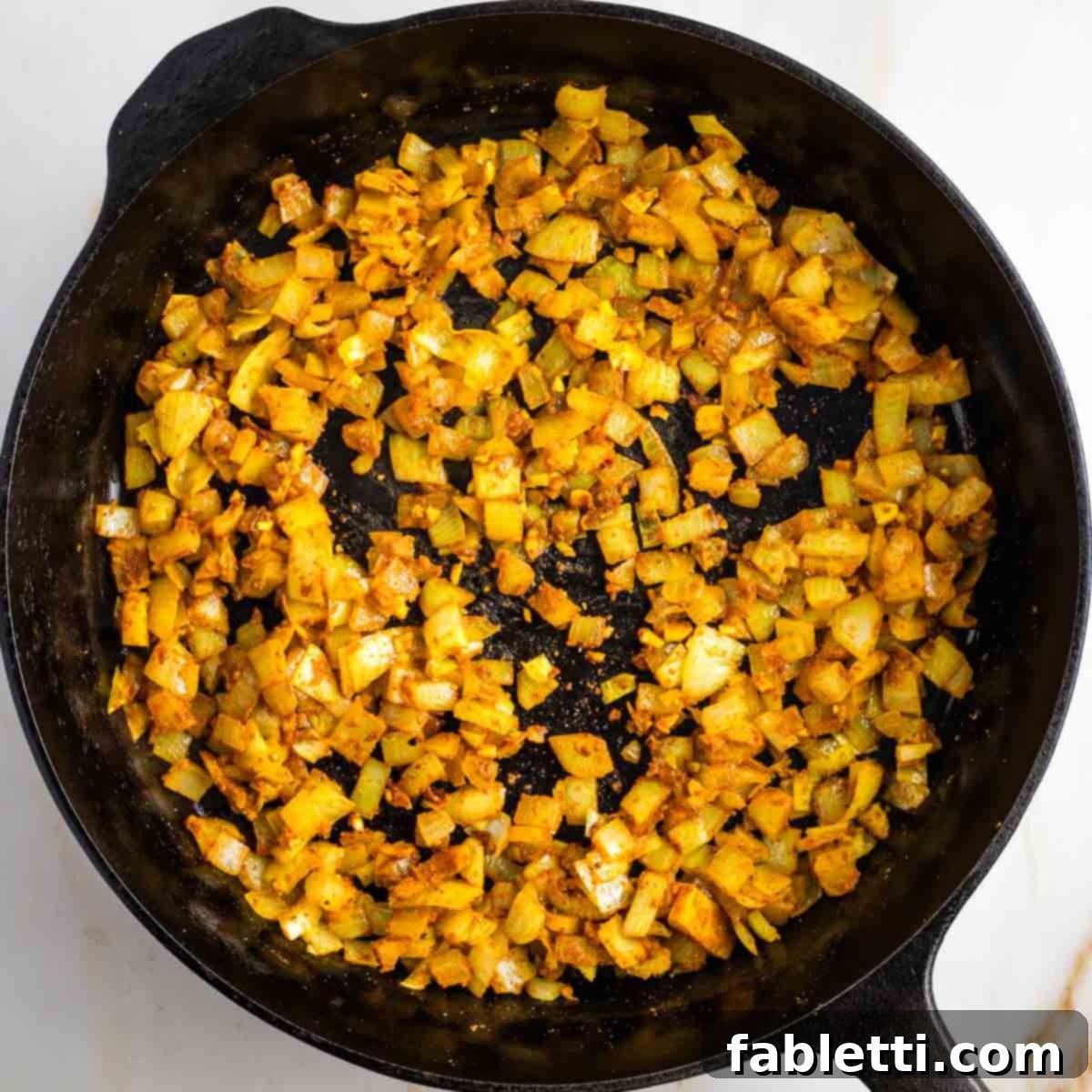 Speedy Skillet Curried Cabbage 5 Fragrant spices being stirred into sautéed onions in a pan.