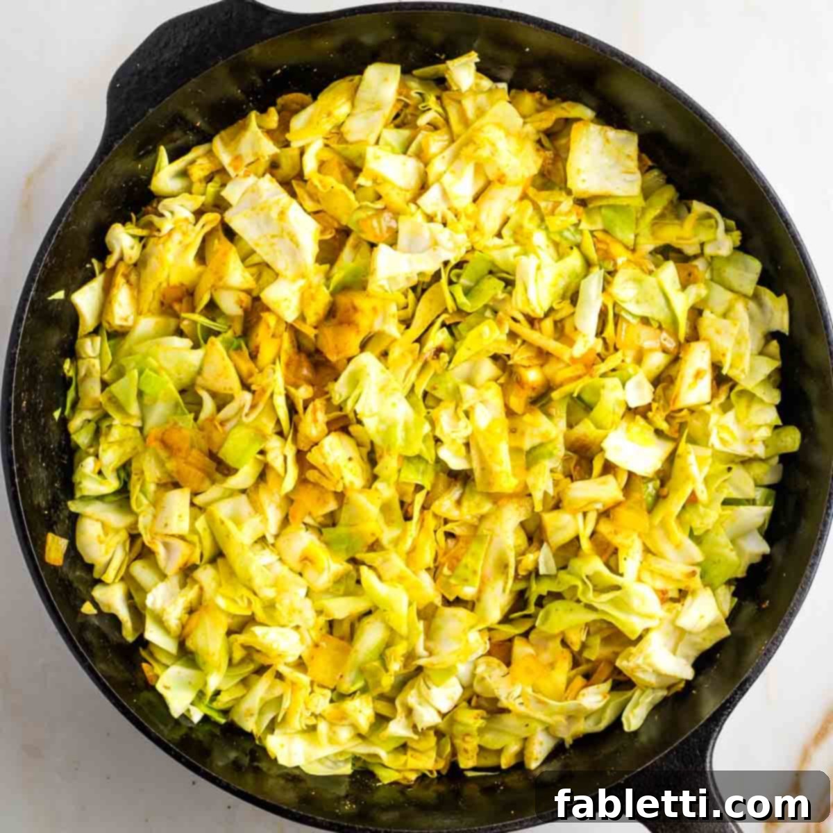 Speedy Skillet Curried Cabbage 6 Chopped cabbage being added to a cast iron skillet with yellow spices and onions.