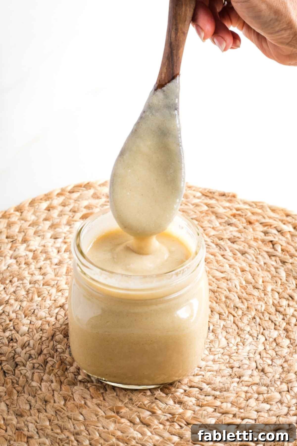 Silky Vegan Bechamel 2 Wooden spoon, coated with bechamel sauce, coming out of a jar, showing how thick sauce is.