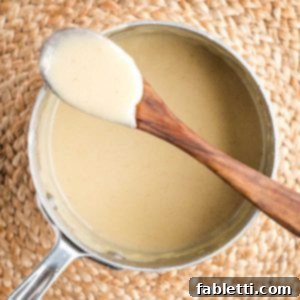 Silky Vegan Bechamel 12 Bechamel sauce clinging to a wooden spoon resting atop a saucepan filled with the white sauce.