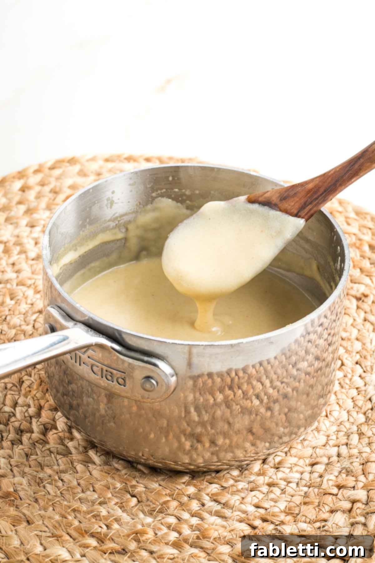 Silky Vegan Bechamel 10 Wooden spoon peeking out of a saucepan full of white sauce to show how thick it is.