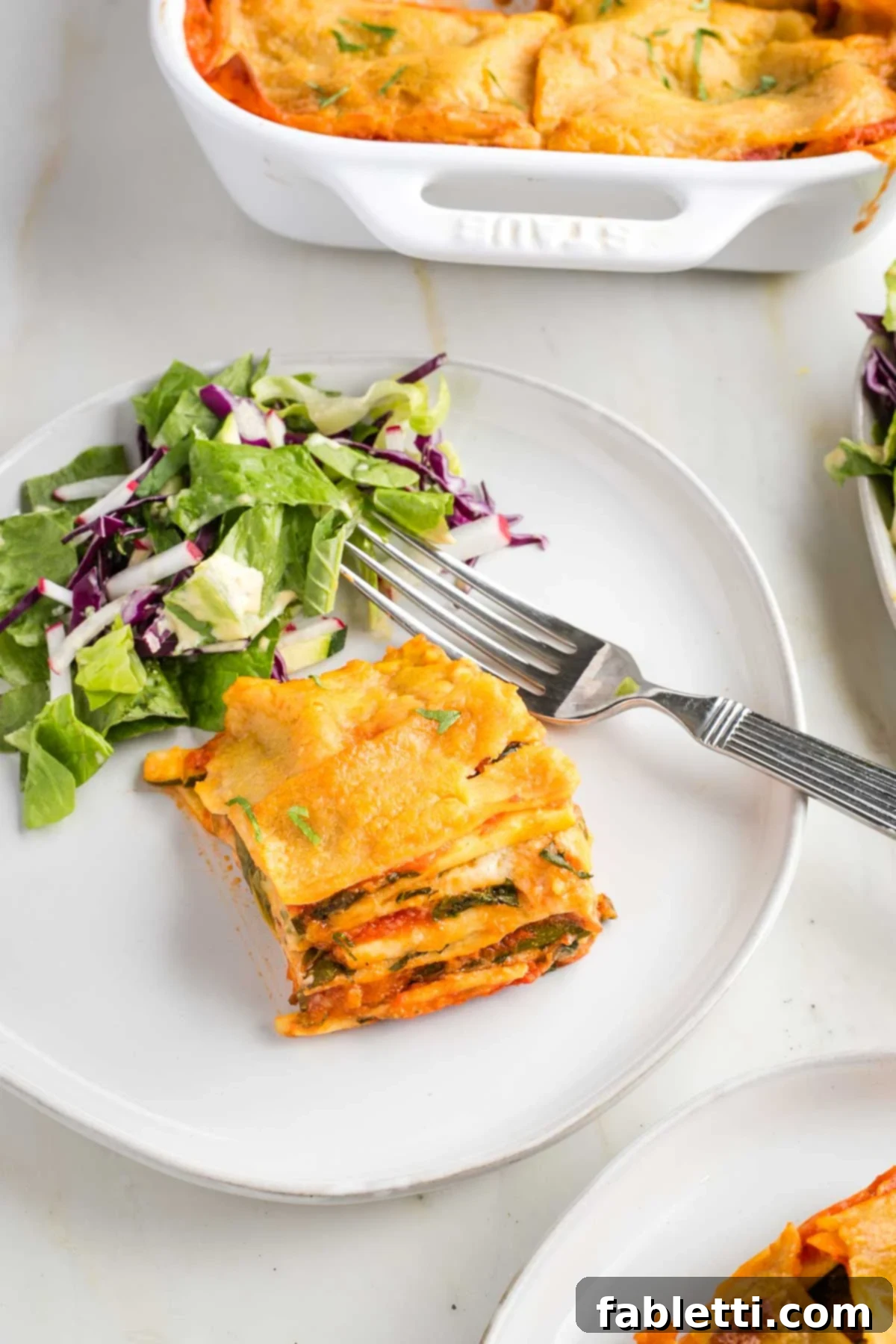 Lush Layers: Gluten-Free Vegan Garden Lasagna 2 Piece of lasagna shown from the side, so you can see layers of red and white sauce, plus spinach and zucchini.