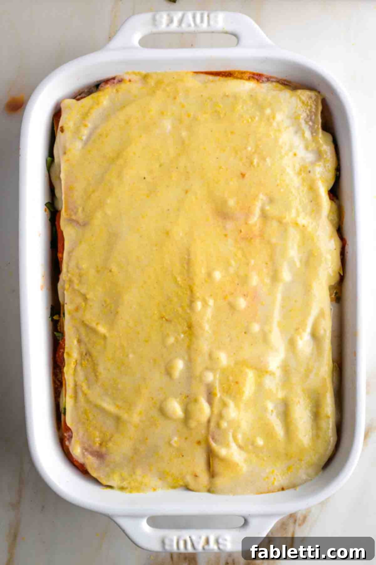 Lush Layers: Gluten-Free Vegan Garden Lasagna 12 Casserole dish layered with sheets of lasagna noodles, red sauce, white sauce, zucchini and greens, ending with bechamel and nutritional yeast.