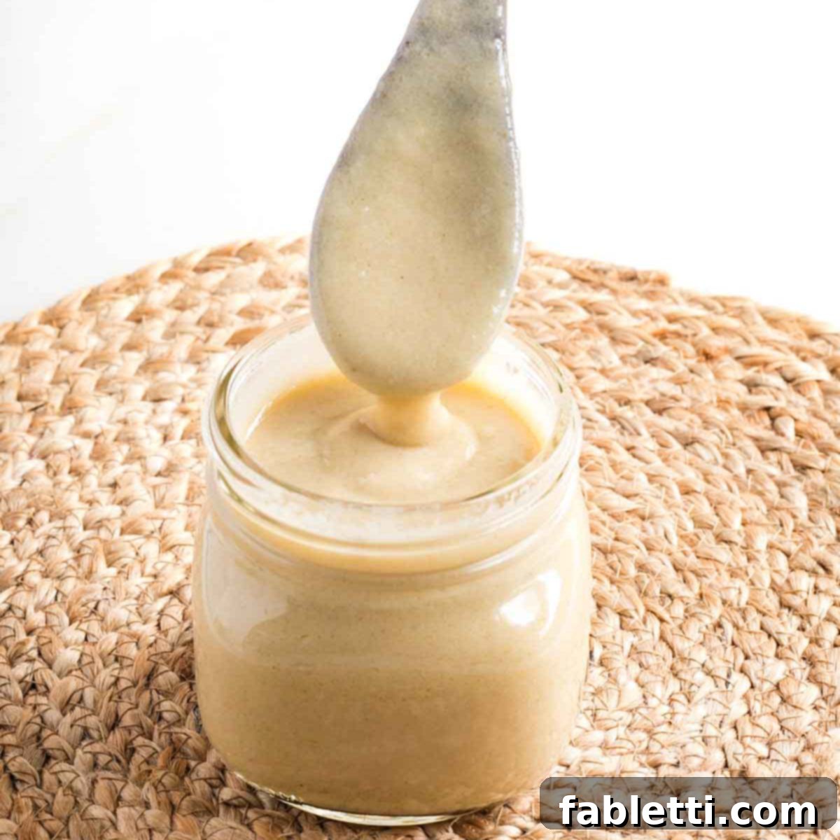 Lush Layers: Gluten-Free Vegan Garden Lasagna 4 Wooden spoon coming out of a jar of bechamel sauce, showing how thick it is.