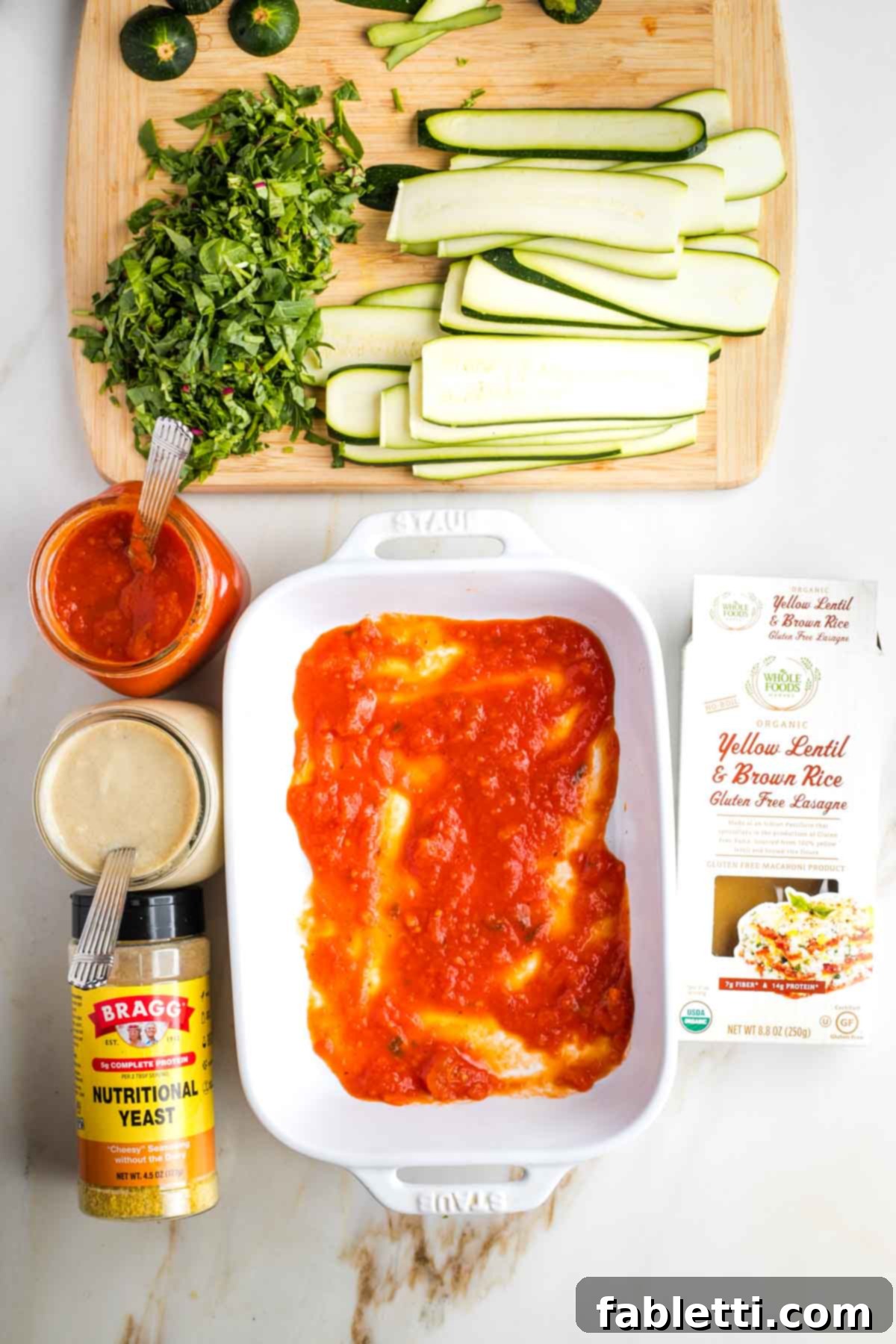 Lush Layers: Gluten-Free Vegan Garden Lasagna 7 Baking dish with marinara sauce, surrounded by ingredients for lasagna.