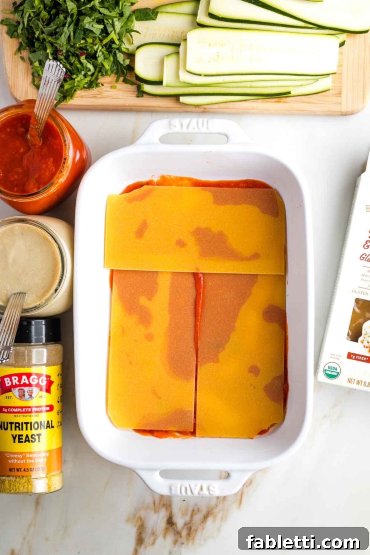 Lush Layers: Gluten-Free Vegan Garden Lasagna 8 Baking dish with a layer of marinara sauce and a layer of uncooked lasagna noodles.