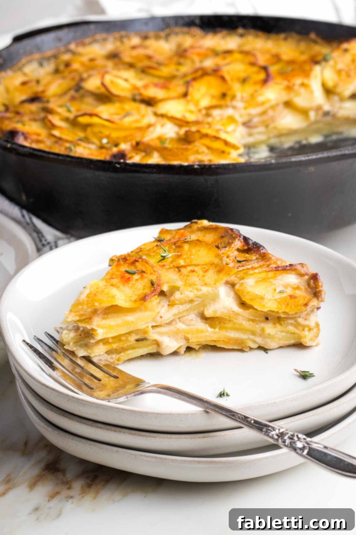One-Pan Dairy-Free Gluten-Free Scalloped Potatoes 2 A perfectly baked slice of dairy-free scalloped potatoes, golden brown and bubbling, being carefully lifted from a cast iron skillet, showcasing its beautiful layers.