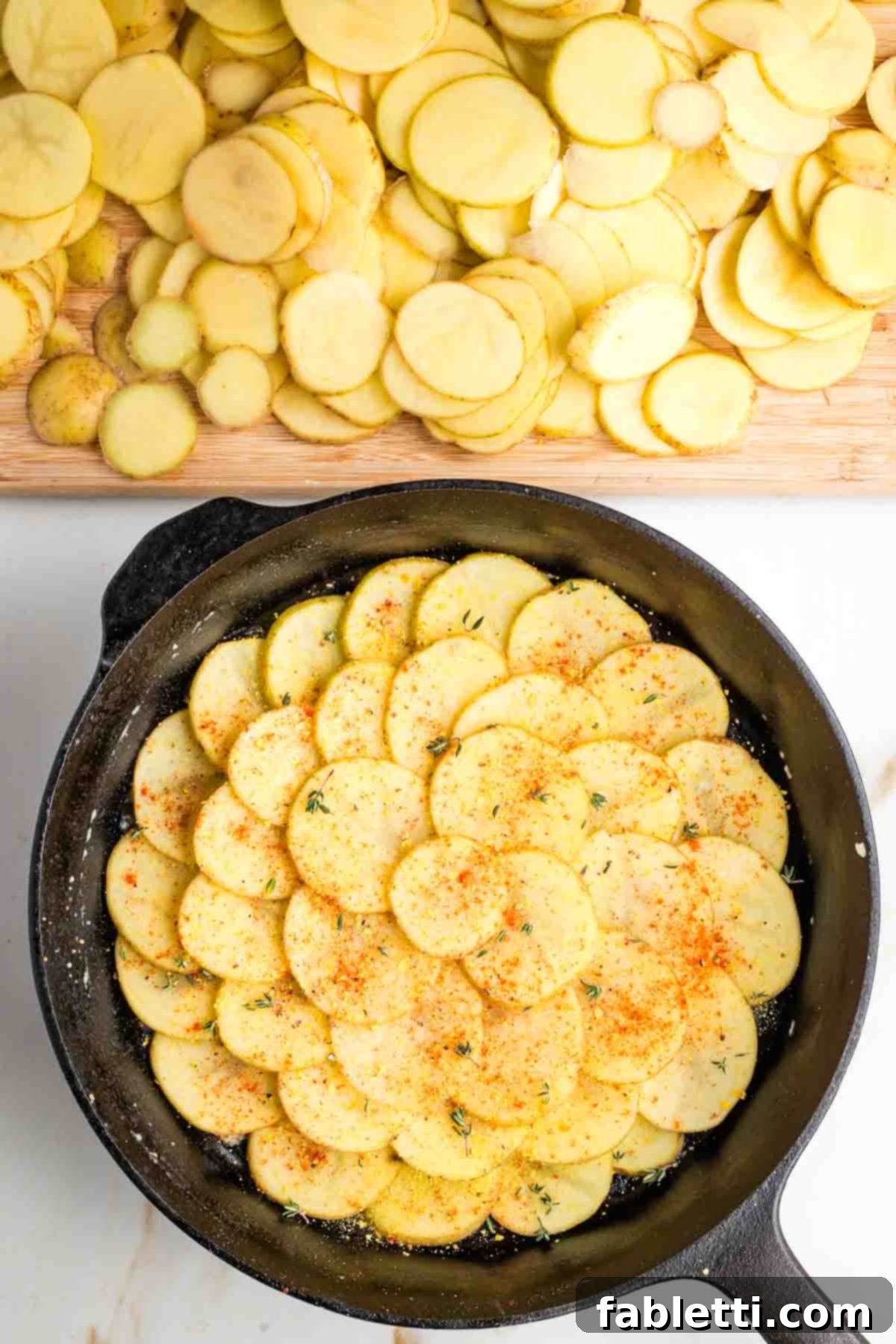 One-Pan Dairy-Free Gluten-Free Scalloped Potatoes 9 Thin slices of potatoes artfully staggered to form a circular pattern in a cast iron skillet, generously sprinkled with paprika, salt, pepper, and fragrant fresh thyme, preparing for the next layer of flavor.