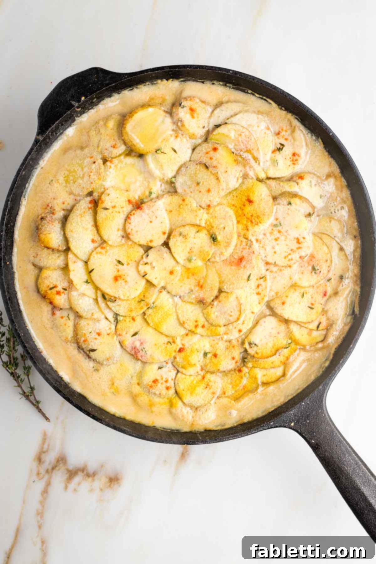 One-Pan Dairy-Free Gluten-Free Scalloped Potatoes 12 Half-baked dairy-free scalloped potatoes in a cast iron skillet, showing the sauce bubbling around the tender potato layers before the final crisping stage.