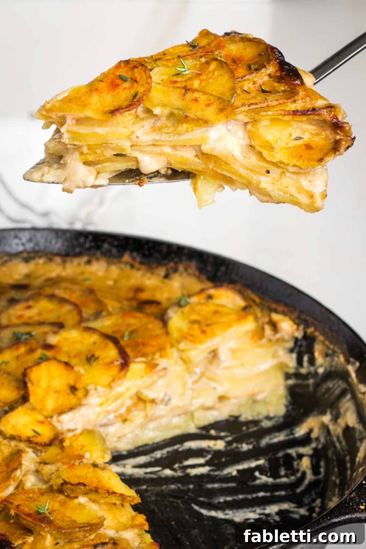 One-Pan Dairy-Free Gluten-Free Scalloped Potatoes 14 A spatula gently lifts a triangular slice of dairy-free scalloped potatoes from a cast iron skillet, revealing the tender, creamy layers beneath the golden-brown crust.