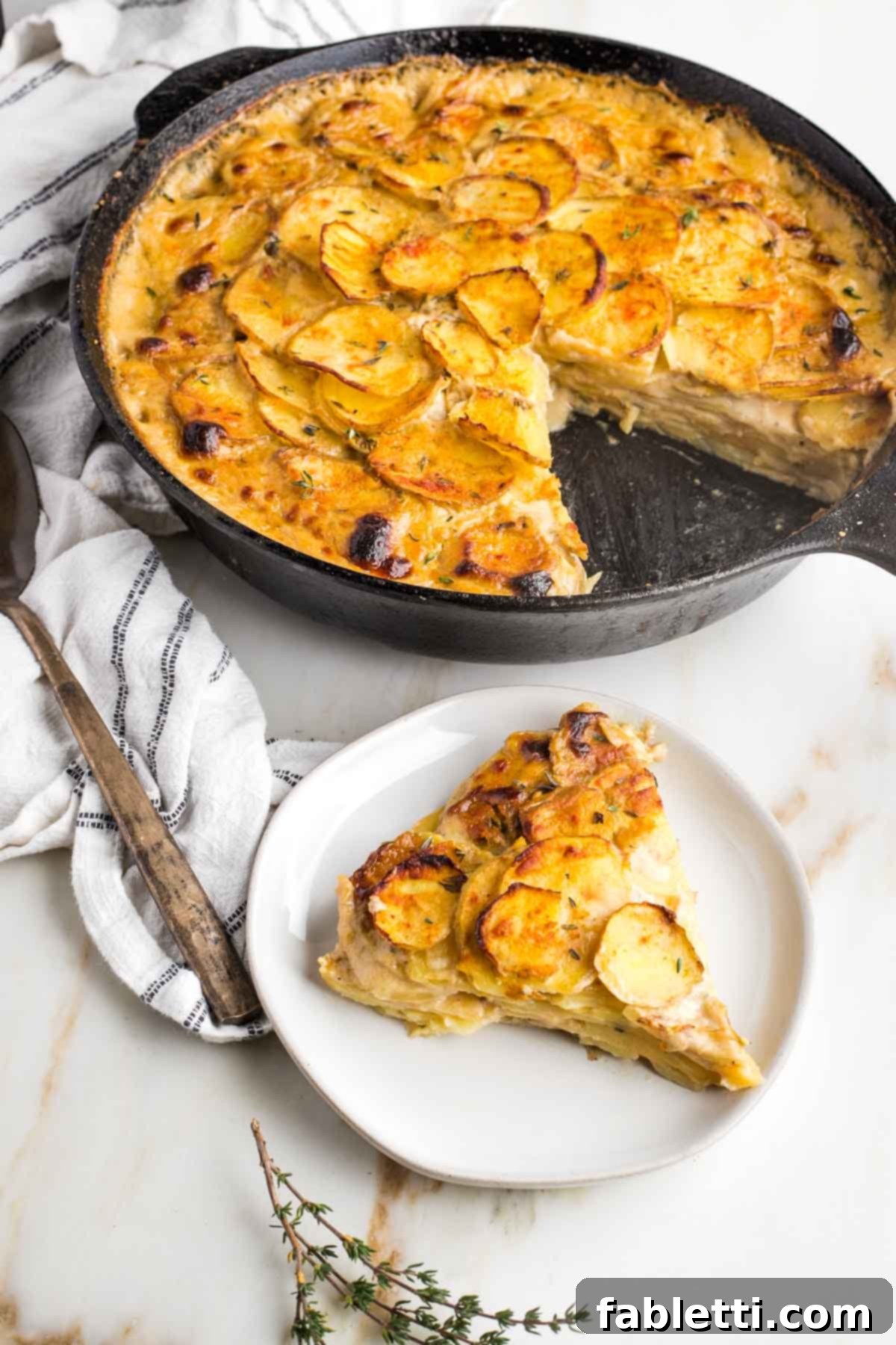 One-Pan Dairy-Free Gluten-Free Scalloped Potatoes 15 A pristine slice of dairy-free scalloped potatoes elegantly presented on a plate, with the bubbling, crisped skillet of remaining potatoes in the background, highlighting the golden-brown top and tender interior.