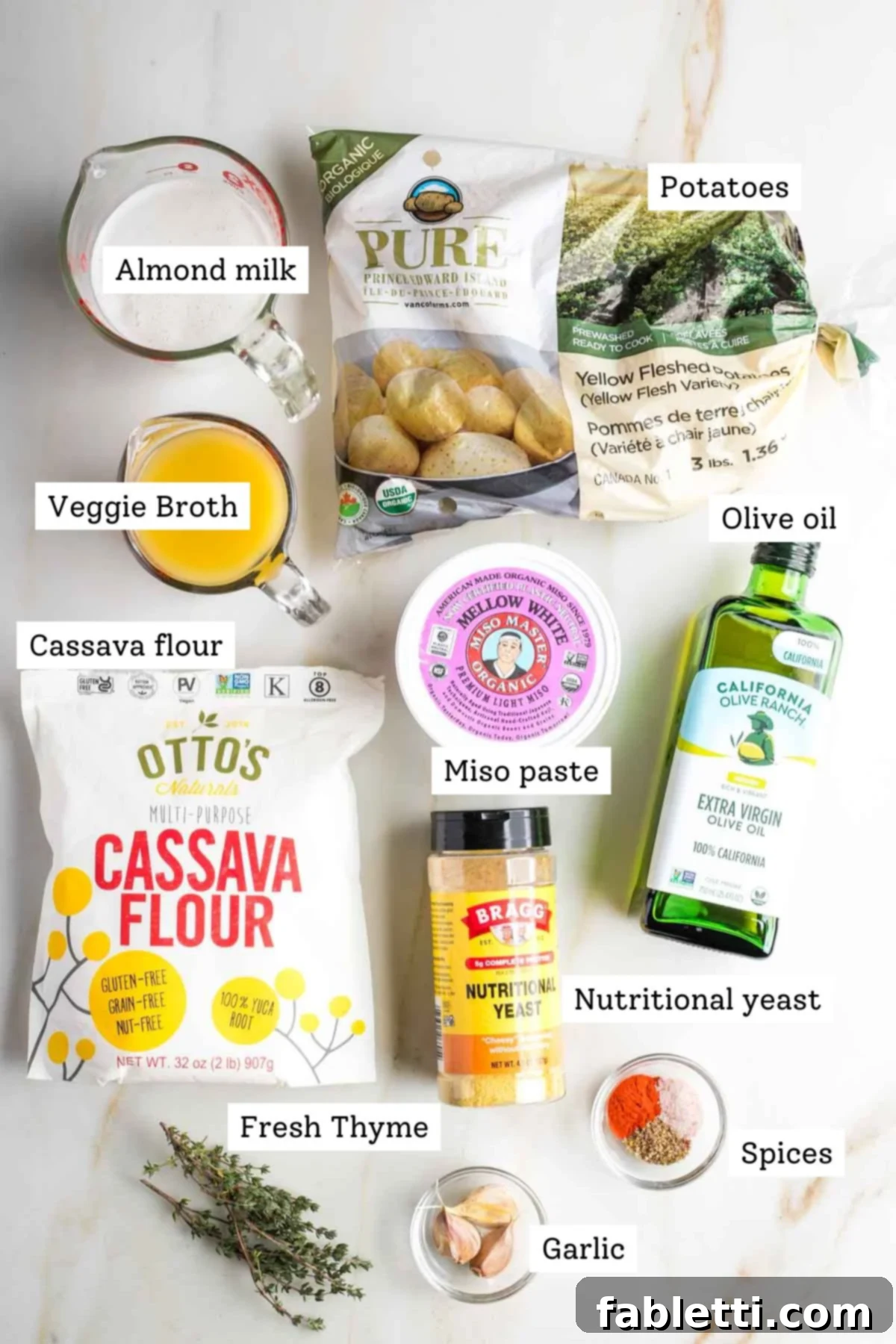 One-Pan Dairy-Free Gluten-Free Scalloped Potatoes 3 A collection of carefully labeled ingredients for dairy-free scalloped potatoes, including fresh miso paste, vegetable broth, plant-based milk, olive oil, cassava flour, vibrant fresh herbs like thyme, aromatic garlic, and various spices.