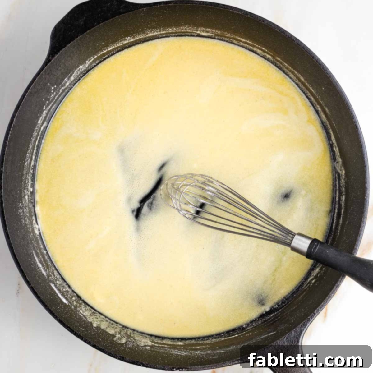 One-Pan Dairy-Free Gluten-Free Scalloped Potatoes 5 The process of whisking a classic white sauce together in a cast iron skillet, showing the sauce gradually thickening and becoming smooth.