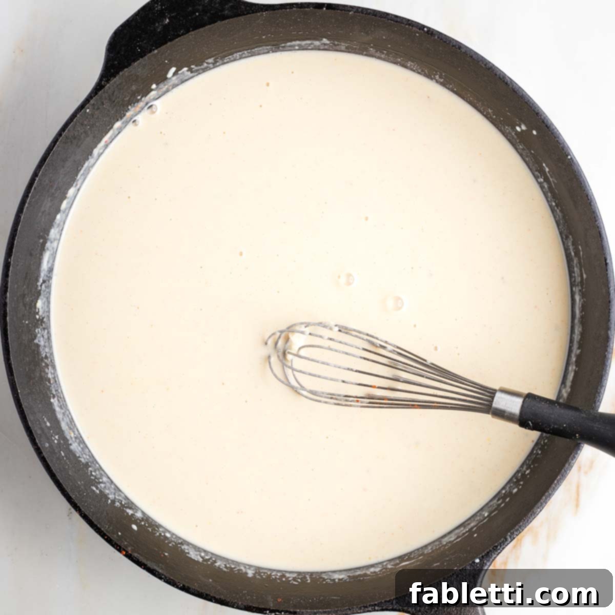 One-Pan Dairy-Free Gluten-Free Scalloped Potatoes 7 A perfectly smooth and creamy white sauce resting in a cast iron skillet, its luxurious texture indicating it's ready for the next step of the scalloped potatoes recipe.