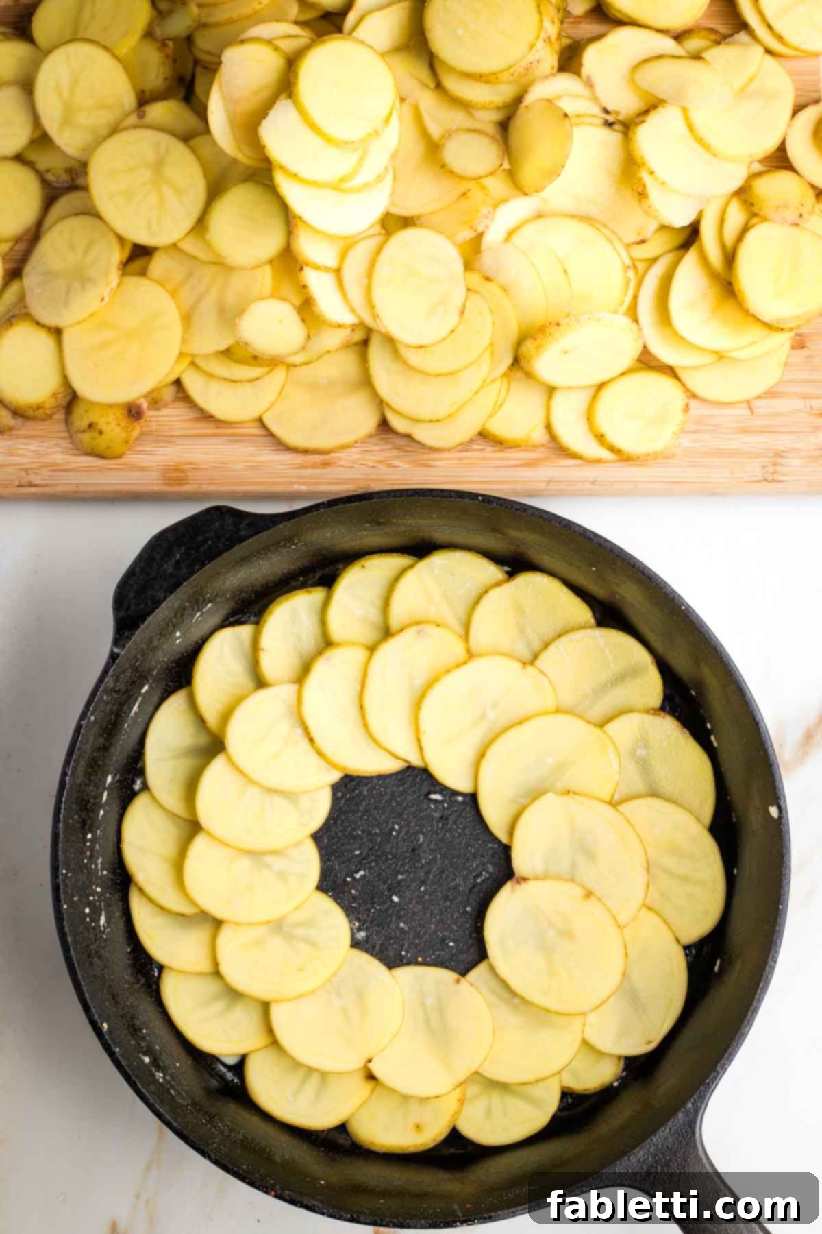 One-Pan Dairy-Free Gluten-Free Scalloped Potatoes 8 Two concentric rings of thinly sliced potatoes meticulously placed into a cast iron skillet, forming the base layer for the scalloped potatoes.