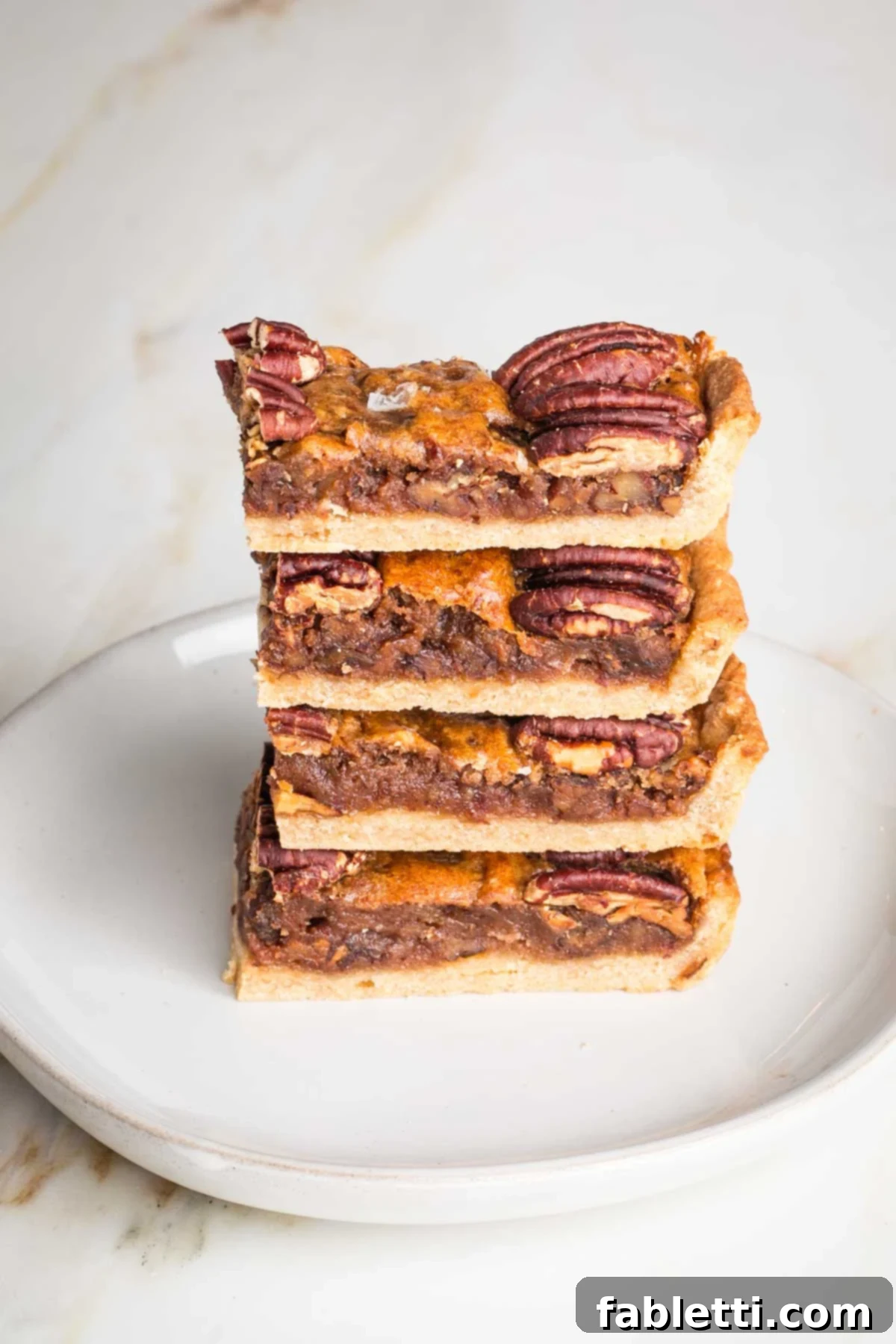 Naturally Sweetened Vegan Pecan Pie Bars 2 Side view of a stack of pecan pie bars, showing layers of crust, chewy filling and pecans on top.