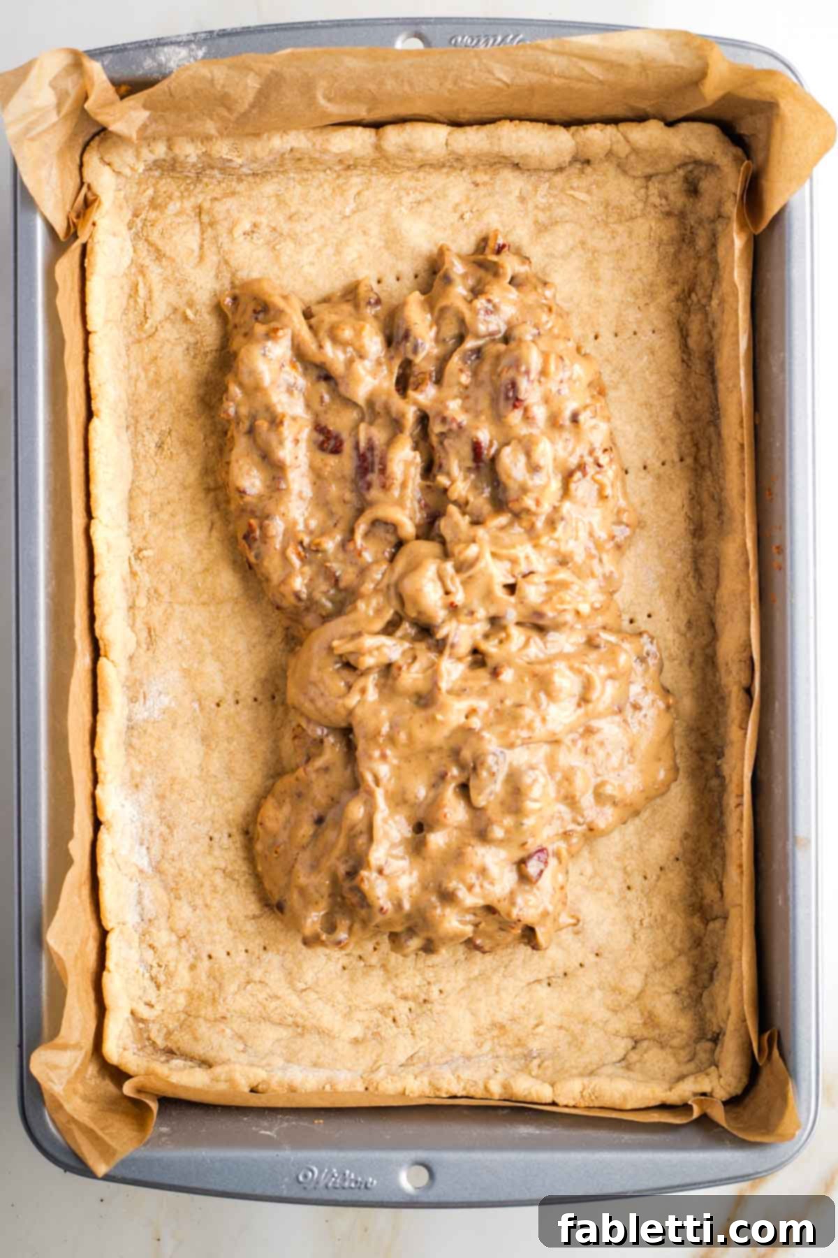 Naturally Sweetened Vegan Pecan Pie Bars 17 Caramel and pecan spread on top of a par baked rectangular pie crust in a baking pan.