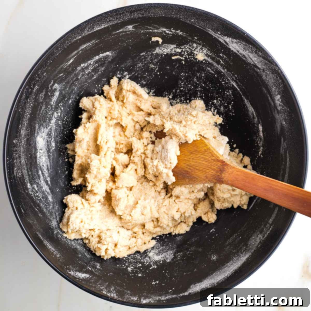 Naturally Sweetened Vegan Pecan Pie Bars 6 Wooden spoon stirring a dough mixture inside a black bowl.