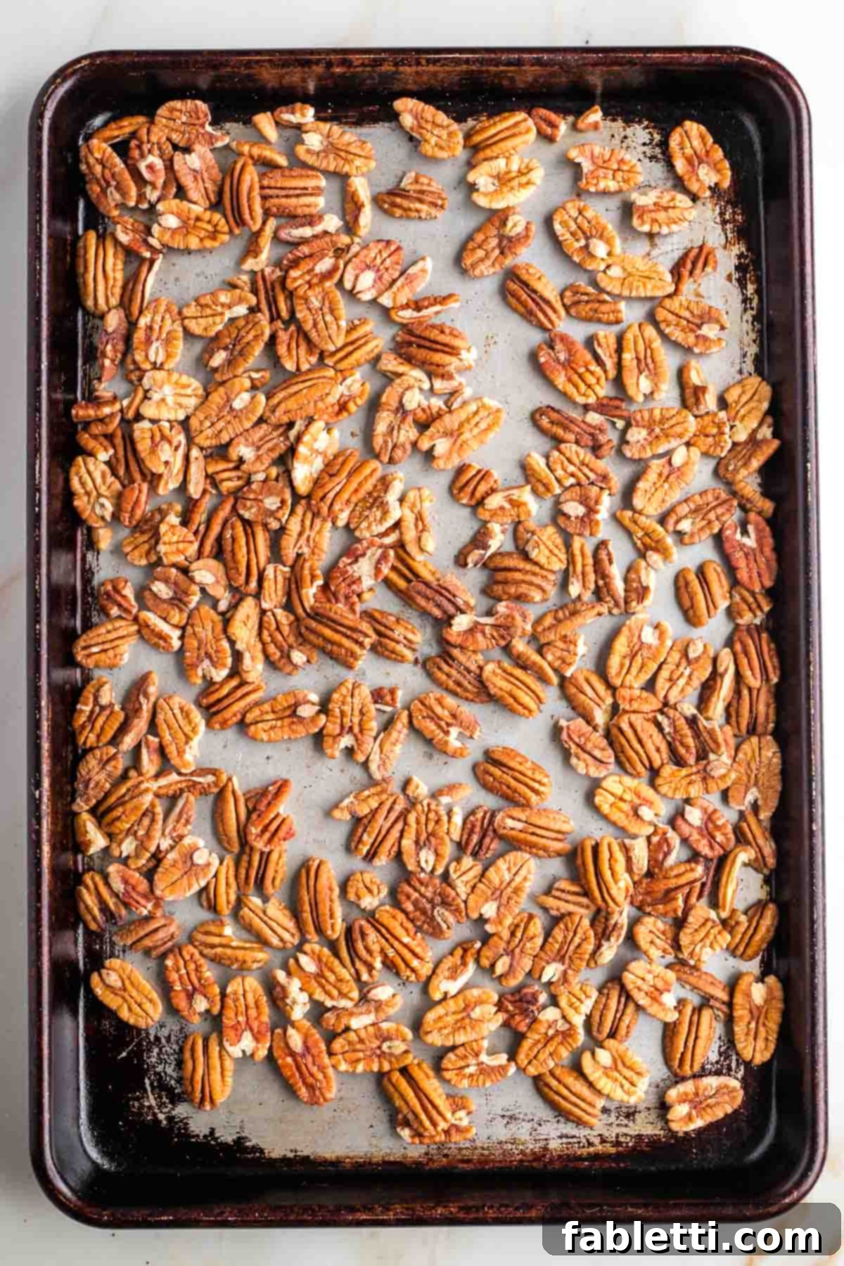 Naturally Sweetened Vegan Pecan Pie Bars 10 Raw pecan halves spread onto a dark baking sheet.