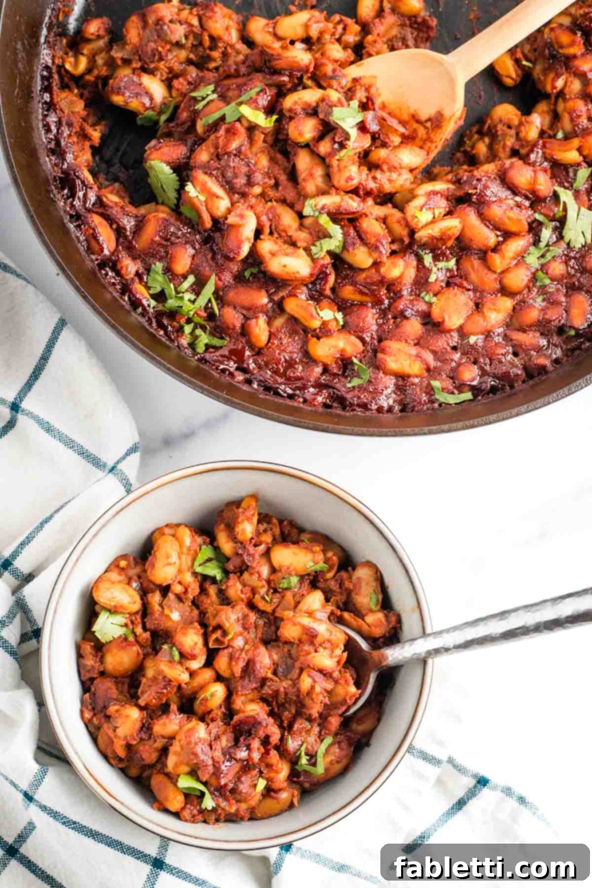 Effortless Skillet Plant-Based BBQ Beans 14 A charming bowl of perfectly baked beans is presented in front of the cast iron skillet they were cooked in, adorned with a sprinkle of vibrant fresh herbs, ready to be savored.