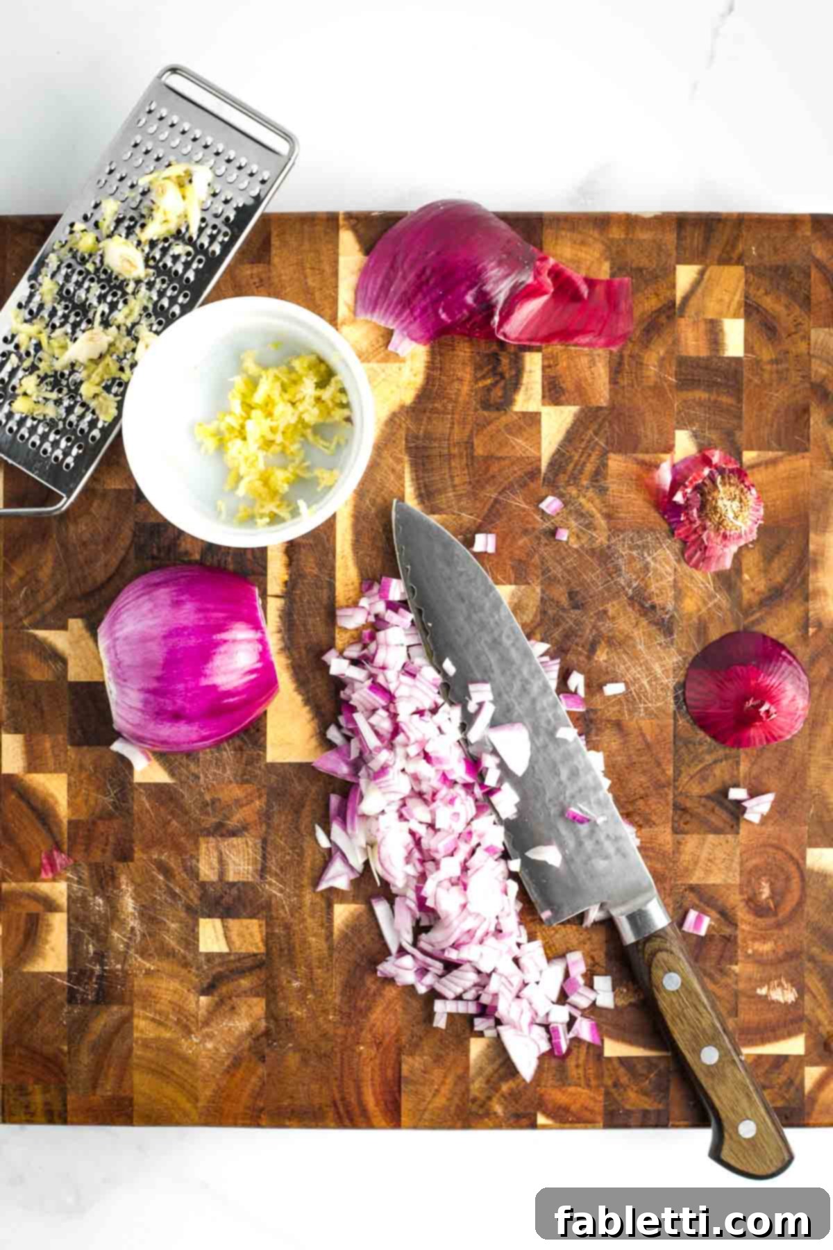 Effortless Skillet Plant-Based BBQ Beans 5 A wooden cutting board with a red onion being diced, alongside a small dish filled with finely grated garlic cloves, illustrating the initial preparation steps.