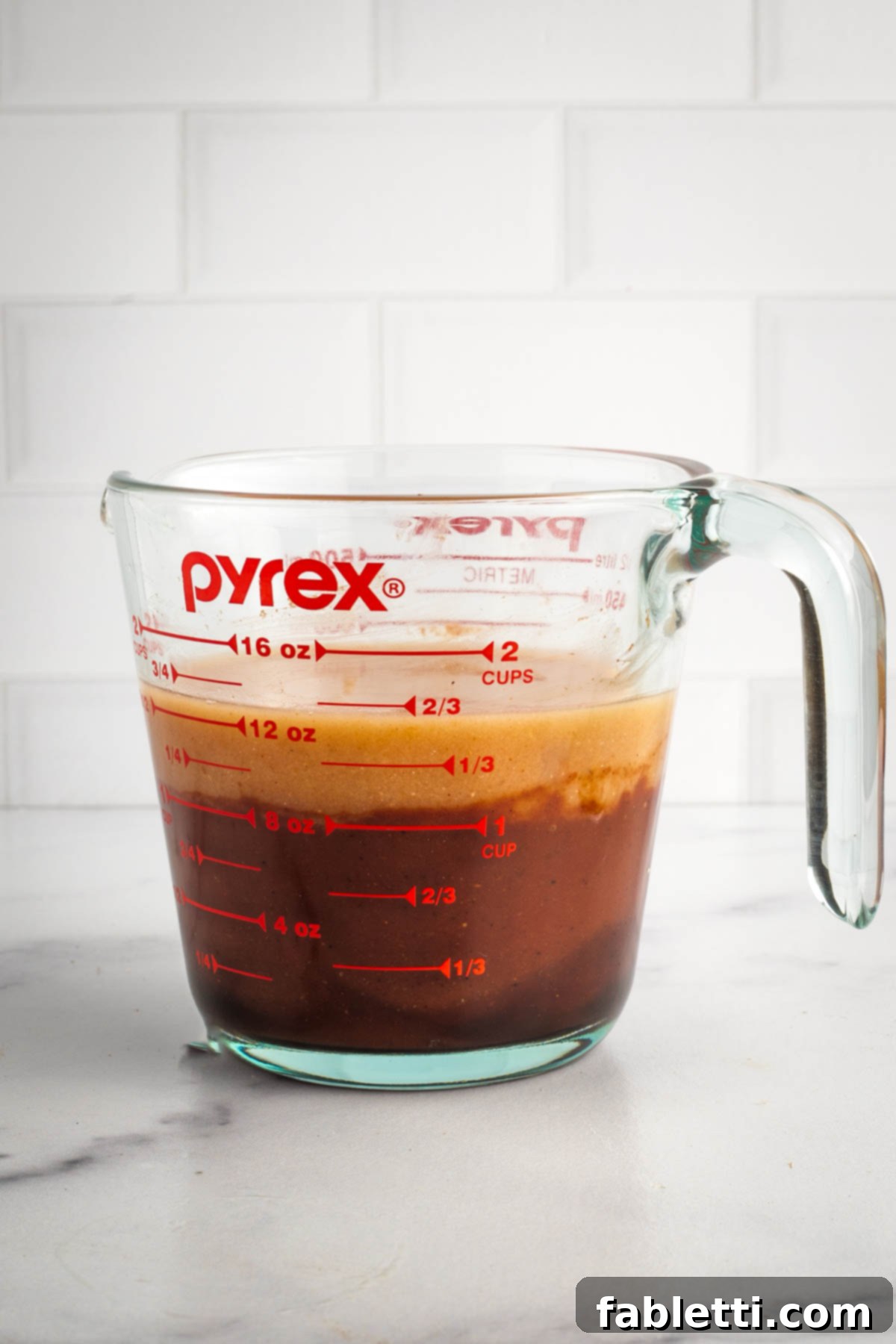 Effortless Skillet Plant-Based BBQ Beans 7 A close-up shot of a measuring cup, with a layer of rich BBQ sauce at the bottom, topped by the recently stirred and diluted miso paste, ready to be fully combined.