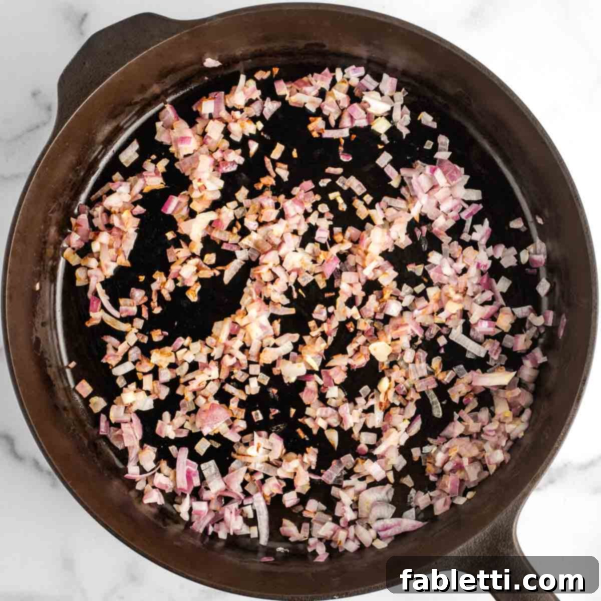 Effortless Skillet Plant-Based BBQ Beans 8 A cast iron skillet holds a vibrant bed of diced red onion, glistening and softened after being sautéed to perfection over medium heat.