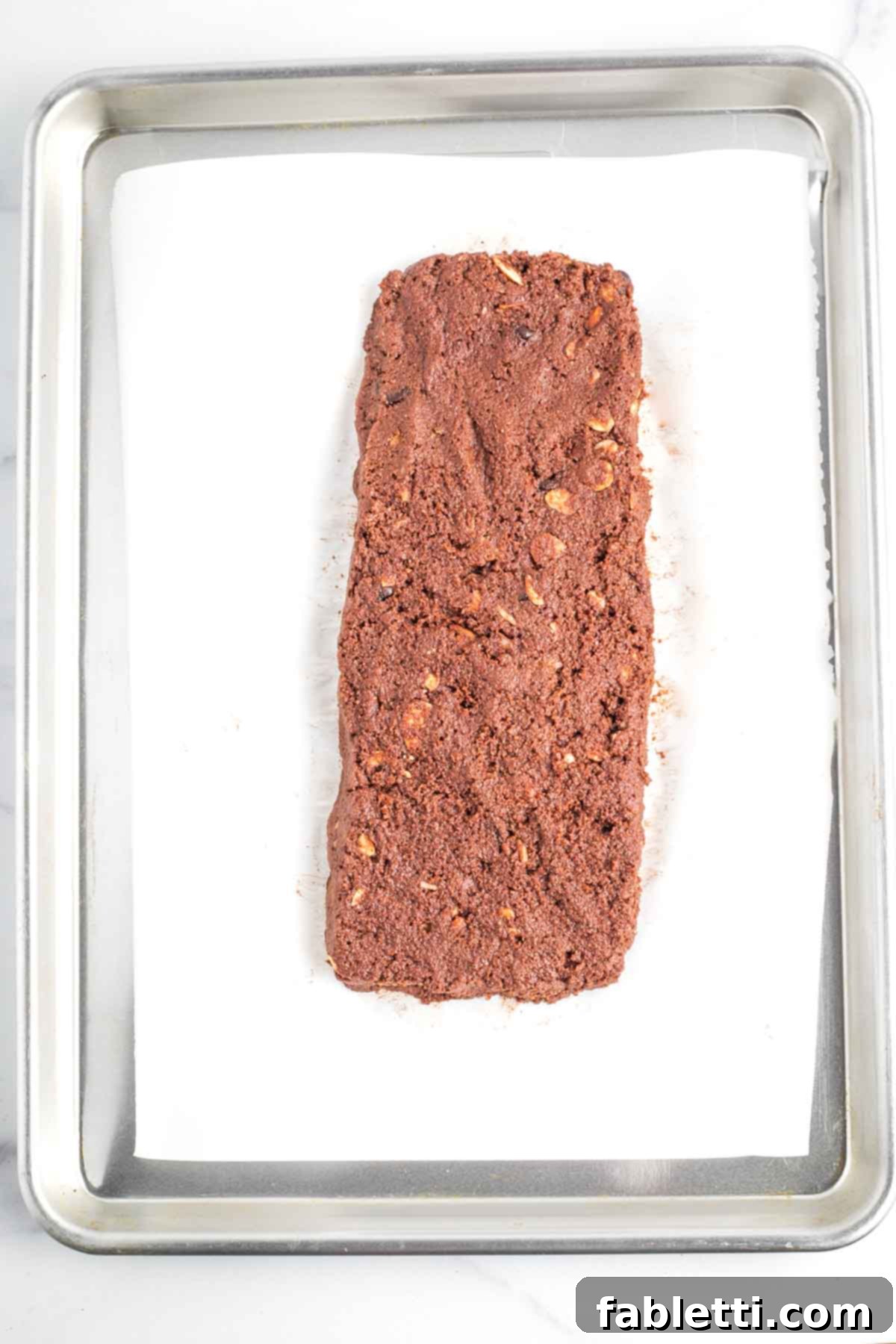 Irresistible Vegan Gluten-Free Chocolate Almond Biscotti 11 Hands shaping a log of chocolate biscotti dough on a parchment-lined baking sheet.